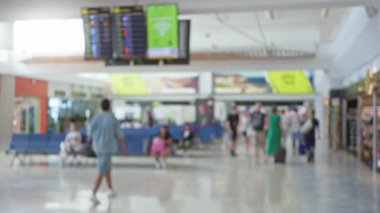 Arka planda uçuş bilgileri olan havaalanı terminalindeki insanlar, dağılmış yolcularla dolu yoğun bir seyahat atmosferini ve bulanık, hareketli bir sahneyi yakalıyorlar.