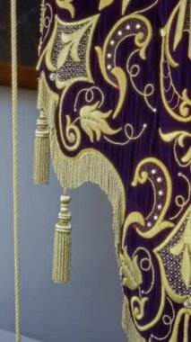Kapalı mekanlarda asılı karmaşık altın işlemeli ve püsküllü kilise halısı zengin mor kumaş üzerinde ayrıntılı dini motifler sergiliyor..