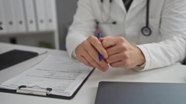 Doktor klinikte notları tartışıyor, beyaz önlüklü adam, boynunda steteskop, el hareketi, iş ortamında sağlık uzmanı, masa başında evrakları olan bir pano..