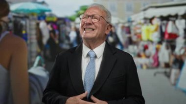 Takım elbiseli, karnı ağrıyan yaşlı bir adam hareketli bir caddede duruyor. Açık hava marketleriyle dolu, şehir yaşamını gözler önüne seriyor..