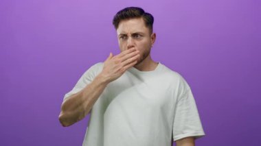 Sakallı genç adam, ağzı inançsızlıkla kaplıyor. İzole bir ortamda, basit mor arka planda poz veriyor. Şaşırdığını ve düşüncelere daldığını gösteriyor..