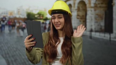 Roma 'da Roma Kolezyumu' nun yanında sarı miğfer takmış açık hava tableti kullanarak mühendislik ve mimarlık becerilerini sergileyen bir kadın mimar videosu..