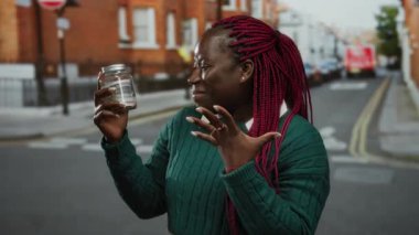 Kadın şehir sokaklarında Amerikan dolarlarıyla dolu cam kavanoz tutuyor, neşe saçıyor, şehir ortamında finansal konsept sergiliyor..