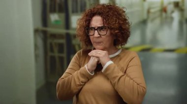 Orta yaşlı, kıvırcık saçlı ve gözlüklü bir İspanyol kadın gün boyunca şehir sokaklarında endişeli görünüyor..