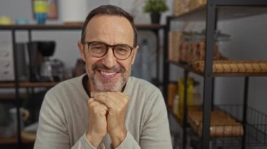 Raflar ve mutfak aletleriyle çevrili, ofis ortamında gülümseyen İspanyol bir adam profesyonel ama gelişigüzel bir ortam sergiliyor..