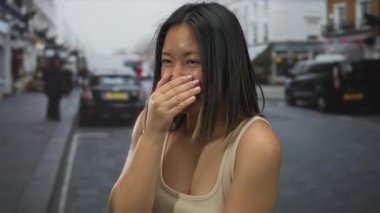 Kadın şehir caddesinde ağzını kapatıyor. Arka planda binalar ve arabalar, şehir manzarası arasında süpriz ve neşe simgeliyor..