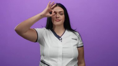Gözünün yanında güzel bir jest yapan bir kadın, canlı mor bir arka plana güvenle gülümsüyor, artı boyutunu ve kıvrımlı vücudunu pozitif bir imajla vurguluyor..