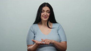 Beyaz bir duvara karşı yalvararak para için el kol hareketi yapan bir kadın, umut dolu ve duygusal bir cazibeyi günlük mavi gömleğiyle taşıyor..