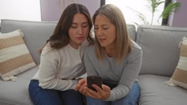 Anne ve kızı evdeki rahat bir kanepede birlikte oturup huzurlu bir oturma odasında sevgi ve iletişim anlarını paylaşıyor ve aileleriyle vakit geçiriyorlar..