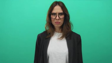 İzole edilmiş yeşil bir zemine karşı kollarını çapraz bağlayan İspanyol bir kadın gözlük takıyor ve gündelik giysiler giyiyor yoğun bir duygusal an yaşatıyor..