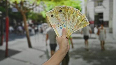 Arka planda bulanık yayalar ve binalar olan kalabalık bir şehir caddesinde Filipin pesoları sergileyen beyaz bir adam..