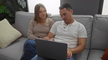 Oturma odasındaki rahat bir kanepede oturan İspanyol çift dizüstü bilgisayarla meşgul oluyorlar, içeride sevgi ve bağ gösteriyorlar..
