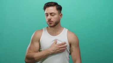 Beyaz kolsuz tişörtlü genç adam, izole edilmiş yeşil arka plan duvarına karşı düşünceli ve düşünceli bir görünüm sergiliyor..