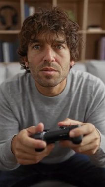 Konforlu bir oturma odasında video oyunları oynayan genç bir adam, bir kontrol cihazını tutarken yoğun bir şekilde odaklanmış, modern bir iç dekora sahip..