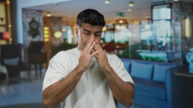 Modern dekor ve ince ışıklandırma ile dolu şık bir otel odasında, günlük beyaz gömlekli yakışıklı bir adam el kol hareketi yapıyor..