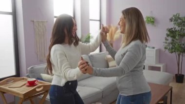 Anne ve kızı sıcak bir oturma odasında birlikte dans ediyor, sıcak bir ev ortamında neşeli bir aile sevgisi ve bağlantı anı yakalıyorlar..