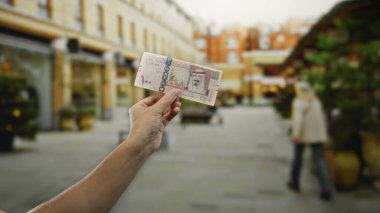Şehir caddesinde elinde Suudi riyal banknotları tutan adam gün ışığında bulanık şehir geçmişine sahip. Ekonomik ya da seyahat kavramını öneriyor..