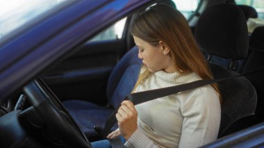Şehir merkezinde bir arabanın içinde emniyet kemeri takan kadın, şehir ortamında güvenlik ve sorumluluk sergiliyor, modern ulaşım ve seyahat odaklarını vurguluyor..