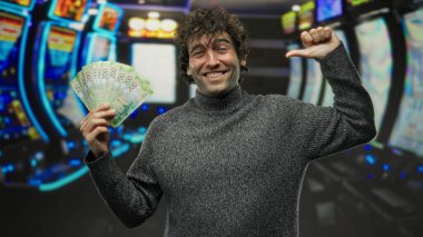 Kumarhanedeki İspanyol asıllı adam kumar makinelerinin yanında Rus rublesi tutarken mutlu bir şekilde kendini gösteriyor. Başarılı bir kumar deneyimi öneriyor..