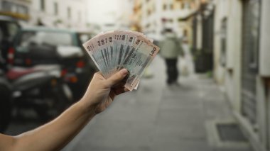 Bangladeşli bir adam işlek bir şehir caddesinde banknot tutuyor, para ve şehir hayatına odaklanmış bir açık hava sahnesini çekiyor..
