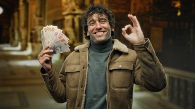 Müzede gülümseyen Türk lirası taşıyan bir adam elinde banknotlar tutarak tatmin ve mutluluğu gösteren bir jest yapıyor..