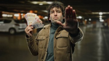 Bir otoparkta İspanyol bir adam bir elinde Türk lira banknotları tutarken diğer elinde de karmaşık bir mali kararın altını çiziyor..