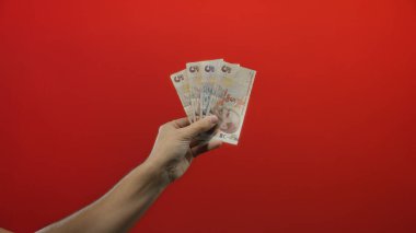 Finansal temalar ve para birimleri kavramlarını vurgulayan, canlı kırmızı izole bir arka plana karşı elinde Türk lirası banknotları tutan adam.