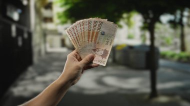 Güney Kore 'yi elinde tutan adam hareketli bir şehir caddesinde elinde banknotlar, canlı bir ortamda kentsel yaşamın ve finansal işlemlerin özünü yakalıyor..