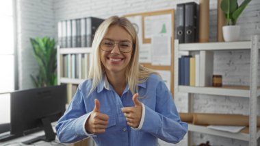 Parlak bir ofis ortamında güvenle gülümseyen bir kadın, bitkilerle ve raflarla çevrili, gözlük takan, mavi gömlekli, pozitiflik ve başarıyı yansıtan.
