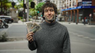 Bir şehir caddesinde elinde İngiliz paundu tutan gülümseyen bir adam İspanyol özellikleri ve şehir yaşam tarzının bir karışımını sergiliyor..