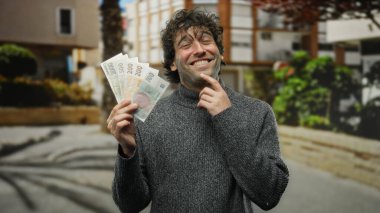 İspanyol adam gülümsüyor ve elinde Czech Koruna banknotları var güneşli bir şehir caddesinde, refah ve canlı şehir ortamında seyahat öneriyor..