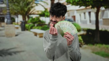 Şehir sokağında elinde Rus banknotları olan bir adam ağaçlar ve bulanık binaları gösteren manzaralı bir arka planda açık havada gülümsüyor..