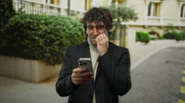 Şehirde akıllı telefona bakarken gergin bir şekilde çivi yiyen genç İspanyol adam, dışarıda gerginlik ve endişe gösteriyor..