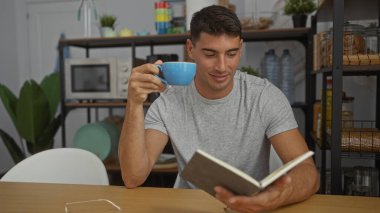 Ofiste kitap okuyan yakışıklı adam, etrafı bitki ve raflarla çevrili kahve içerken, iş yerindeki sakin ve rahat havayı yansıtıyor.