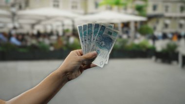 Restoran terasında elinde Polonya parası tutan bir adam var. Arka planda sokak ve kahve müşterileri var. Polonya 'daki ticareti sergiliyorlar..