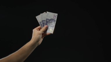 İsveç Krona banknotlarını elinde tutan adam, izole edilmiş siyah arkaplan üzerinde, finansal tema ve kavramları gösteren odaklanmış, karanlık bir ortamda para gösteriyor.