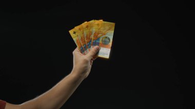 Siyah arka plan üzerinde İsviçre banknotları tutan adam dramatik izole bir ortamda para birimi ayrıntılarını sergiliyor..