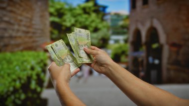 Şehir sokaklarında elinde Şili pezosu olan bir adam, açık bir şehir ortamında para ve yatırım odaklı bir tablo çiziyor..