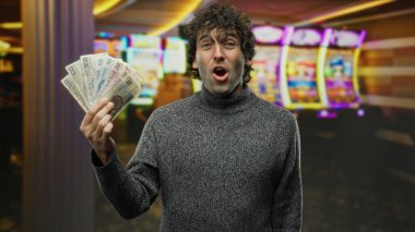 İspanyol adam heyecanlı bir şekilde kumarhane kumar makinesinin yanında Czech Koruna banknotlarını tutuyor. Canlı bir kumar ortamında zafer ve servet hissini vurguluyor..