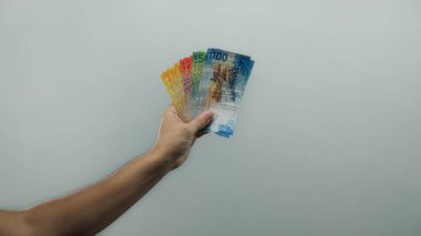 Adam, beyaz izole edilmiş arka plana karşı İsviçre frangını elinde tutuyor. Duvarın üzerinde çeşitli renkli banknotlar vurguluyor..