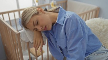 Yatak odasında bir beşiğin yanında uyuyan bir kadın, yorgunluk ve sakinliği ifade eder, sakin bir iç mekan yakalar, güzellik ve sükuneti ön plana çıkarır yumuşak ışıkla filtreleyerek.