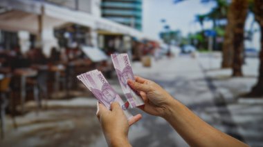 Açık hava kahve dükkanında Endonezya rupiasını sayan eller iş alışverişine işaret ediyor.