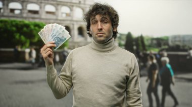 Roma 'daki Roma Kolezyumu' nun önünde, arka planında şehir merkezi olan bir sokak dekoruyla, Polonyalı zloti banknotları tutan İspanyol bir adam..