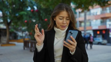 Şehir parkında telefona bakarken parmaklarını çapraz yapan bir kadın şehir sokaklarında umut ve beklenti taşıyor..