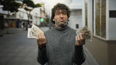 İngiliz sterlinli banknotları elinde tutan İspanyol bir adam açık bir şehir caddesinde duruyor, kendine güvenen bir ifadeyle şehir ortamında finansal başarı sergiliyor..