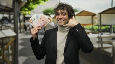 Bir şehir caddesinde dikilen İspanyol bir adam, Thai banknotlarını tutarken el kol hareketleri yapıyor, neşeli bir ifadeyle finans ve seyahat temaları sergiliyor..