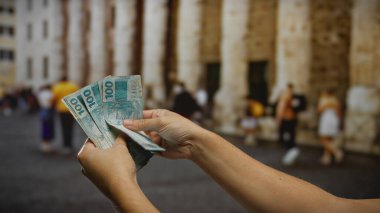 Kalabalık bir caddede Brezilya banknotları tutan adam, para ve ticaret odaklı canlı bir şehir iş sahnesi çekiyor..