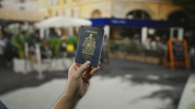 Elinde Kanada pasaportu olan bir adam şehir dışındaki kafe terasına karşı seyahat etmeyi simgeliyor..