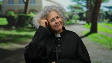 Dini giyinmiş gri saçlı kadın güneşli bir parkta bir fikir jesti yapıyor..