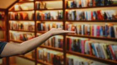 Adamın eli, arka planda raflarda sayısız kitap bulunan kapalı bir kütüphane ortamında eğitim ve bilgi paylaşımını öneriyor..